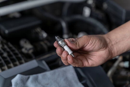 A close-up of a hand holding a spark plug, symbolizing routine vehicle maintenance and DIY auto care.