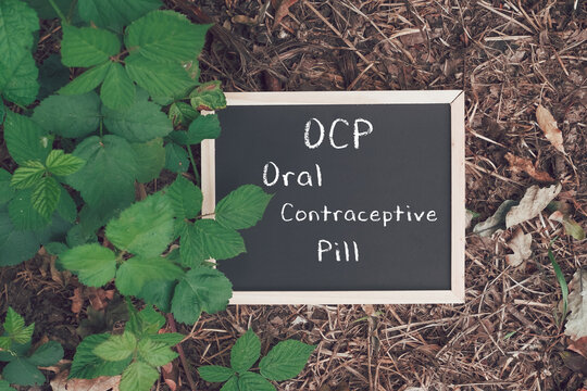 Chalkboard sign displaying OCP, Oral Contraceptive Pill surrounded by lush green foliage
