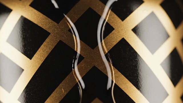 Abstract gold geometric pattern on a sleek black surface with a glistening liquid drop moving across.