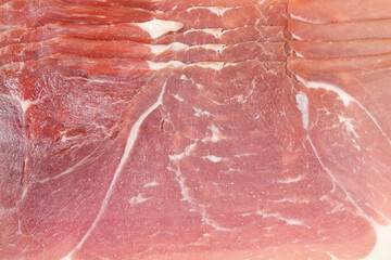 A close-up, detailed shot captures the delicate texture and marbling of several thin slices of dry-cured prosciutto or Italian ham layered together