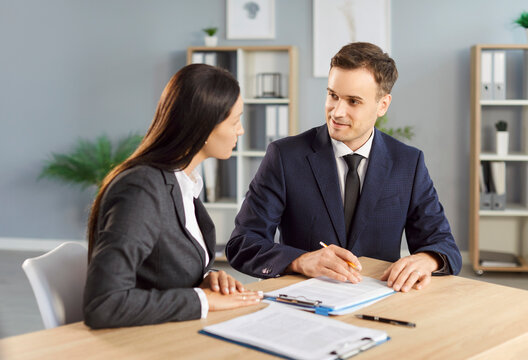 Two confident business people man and woman at work in office. Young company employees sitting at the desk with documents on workplace having discussion and going to sign a contract. - Powered by Adobe