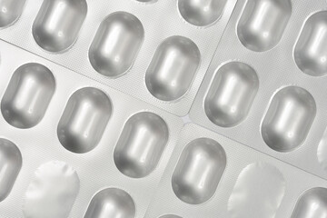 A diagonal close-up shows multiple silver blister packs with rows of oval capsules, some empty, creating a repetitive pattern against a light gray background