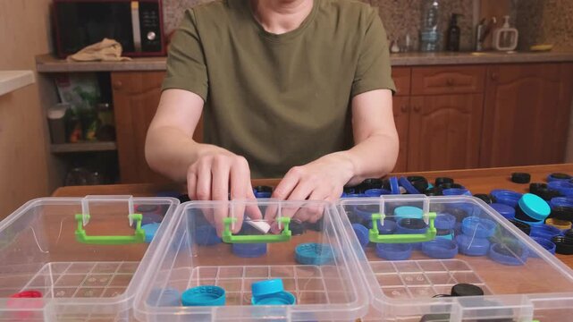 Adult carefully places blue and black lids into separate sections of clear bins, demonstrating simple color coded system for preparing caps before drop off at recycling center