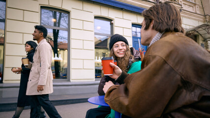 Friends enjoying warm coffee and casual conversation outside city cafe in winter. Concept of seasonal lifestyle branding, cafe marketing, social visuals and modern urban community storytelling.