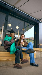 Friends relaxing with takeaway coffee outside neighborhood cafe in winter. Concept of...
