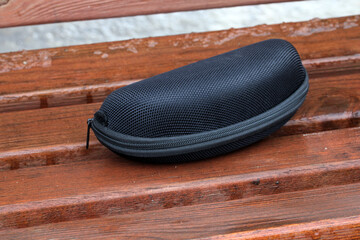 Black hard shell sunglasses case resting on wet bench