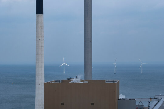 Industry on the sea near Copenhagen contrasts with wind turbines and clean power infrastructure, linking energy and environment, sustainability and climate action through visible contrast