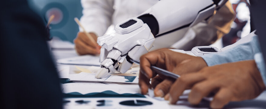 A futuristic robot arm assists professionals in analyzing business reports and data in a modern workspace, showcasing collaboration and technological innovation.Noogenesis