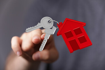 Close up of a hand holding keys with a house keychain. Represents homeownership, new beginnings, and the dream of owning property. Focus on the