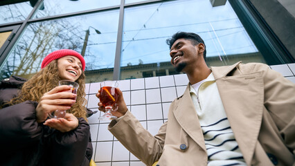 Friends toasting warm drinks together on a winter street. Concept of seasonal cafe branding, social...
