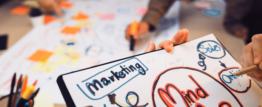 A diverse team engages in a creative brainstorming session, utilizing colorful notes and mind maps to develop innovative marketing strategies and enhance collaboration. SACTR - Powered by Adobe