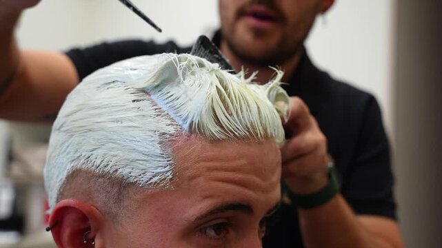 Tight close-up of hairdresser using comb to separate sections where bleaching powder is already applied