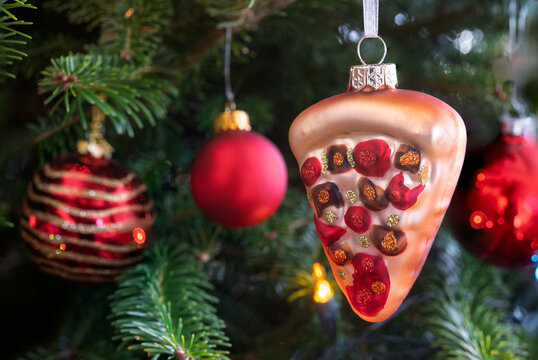 A pizza slice glass ornament hanging in a Christmas tree.