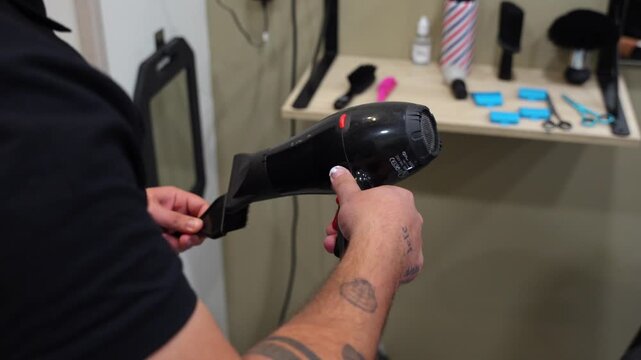 Close shot of hairdresser using hair dryer to blow a neck duster brush and other tools with shelf in background