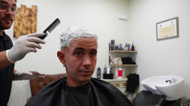 Close-up of hairdresser using a comb to test bleaching powder dryness on client&rsquo;s hair as they laugh