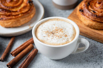 Cappuccino coffee with cinnamon in white porcelain cup and sweet cinnamon raisin bun