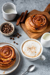 Cappuccino coffee with cinnamon in white porcelain cup and sweet cinnamon raisin bun