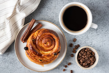 Sweet raisin cinnamon bun and cup of coffee on grey stone background