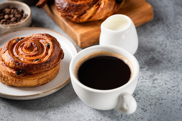 Black coffee in white porcelain cup and sweet puff pastry bun with cinnamon and raisins