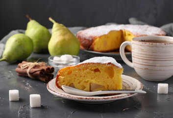 Pie with pears with cut piece and a cup of tea on gray background.