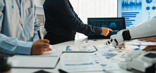 A diverse business team is engaged in data analysis, combining human insights with robotics technology in a modern office setting to drive informed decisions.Noogenesis
