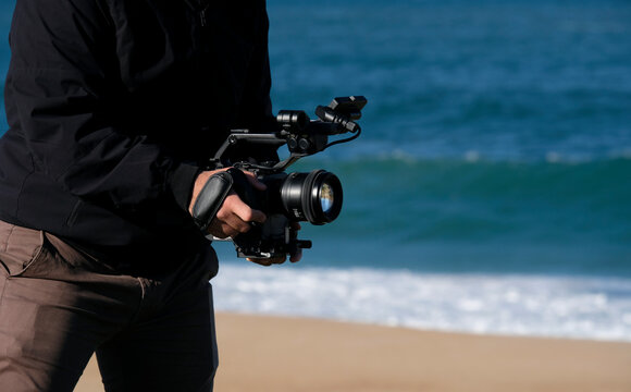 Cameraman filming at the beach on a sunny day with a DSLR camera