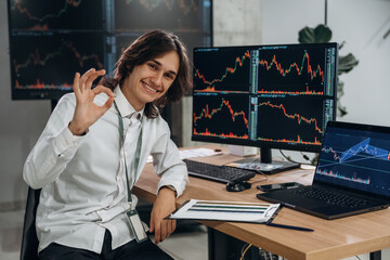 Real time monitoring graphs are on the screens. Young man is sitting in the office with multiple displays of stock market data