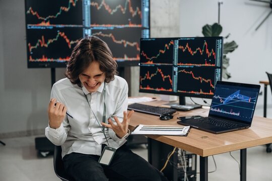Young man is sitting in the office with multiple displays of stock market data