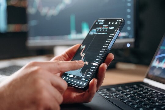 Detailed close up view of man's hands that is holding smartphone with stock market crypto information