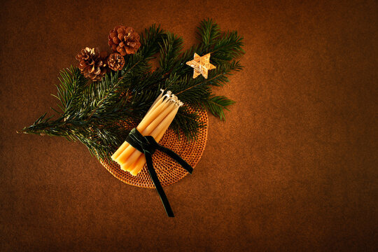 D&eacute;coration de No&euml;l, branche de sapin vert, trois pommes de pin, un fagot de bougies en cire naturelle entour&eacute; d&rsquo;un ruban en velours vert fonc&eacute;, une &eacute;toile en paille, vue du dessus, fond brun fonc&eacute;