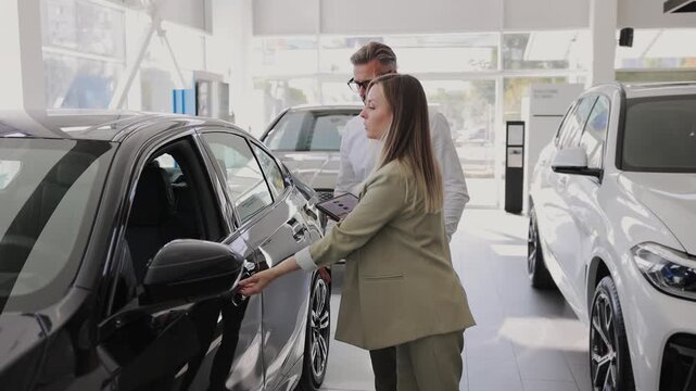 Man customer male buyer client wear white shirt talk with female seller clerk chooses auto wants to buy new automobile in car showroom vehicle salon dealership store motor show indoor. Sales concept