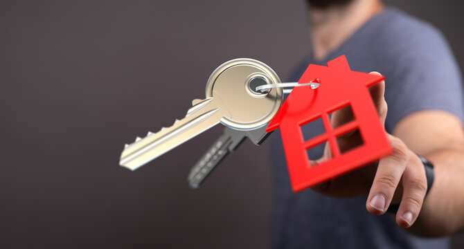 A hand holding keys and a house-shaped keychain. Real estate concept, homeownership, new house purchase and mortgage concept. Investment concept