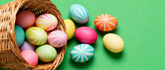 Colorful pastel easter eggs with geometric patterns spill from wicker basket onto bright green background, evoking spring celebrations
