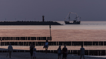 SUNSET OVER THE SEACOAST - Tourists are walking along the beach and a small pleasure boat sails...