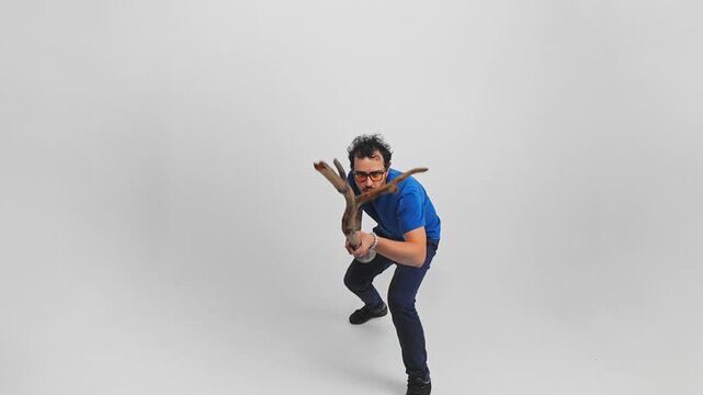 Man portrays a primitive man and defends himself with a stick filmed in a studio on white background. Slow motion of young adult Caucasian man holding a log in his hands and protecting like a caveman.