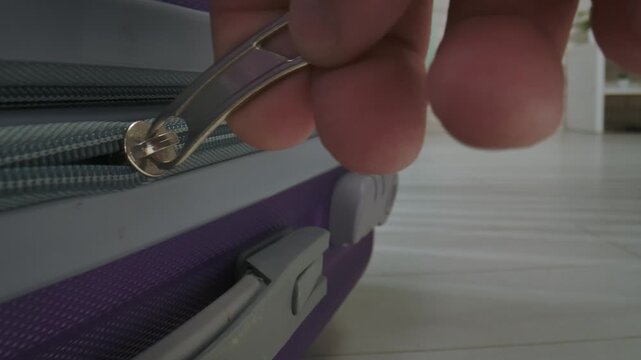 A hand fastens a suitcase in a bright room