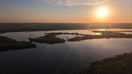 Aerial view of a lake surrounded by land at sunset with a bright sun