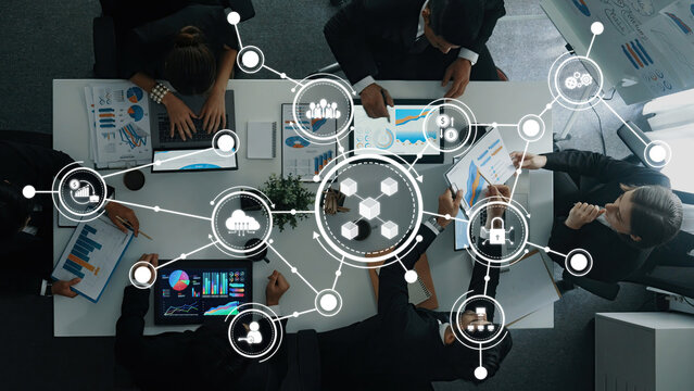 A top-down view of a business meeting showcasing professionals discussing strategies with digital connectivity elements and data visualization to enhance collaboration. Amity