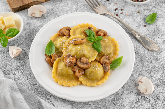 Tradition homemade Italian ravioli pasta with ricotta, mushrooms and parmesan cheese in a white plate on a concrete background. Top view.
