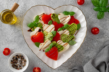 Heart-shaped caprese salad with mozzarella, tomatoes, avocado and basil. A salad for Valentine's Day or Mother's Day. Top view, copy space.