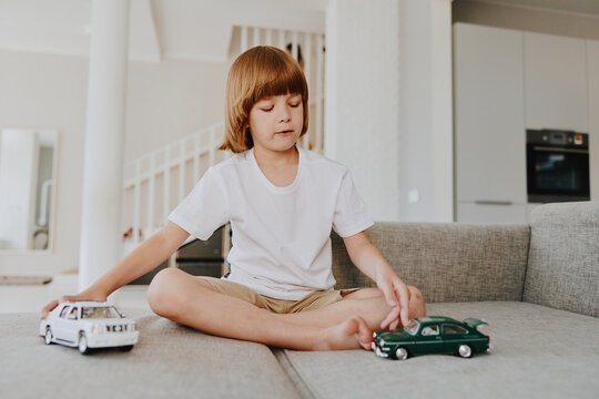 A focused boy sitting on a sofa, playing with toy cars in a bright living room filled with natural light. His playful imagination brings joy and creativity to life.