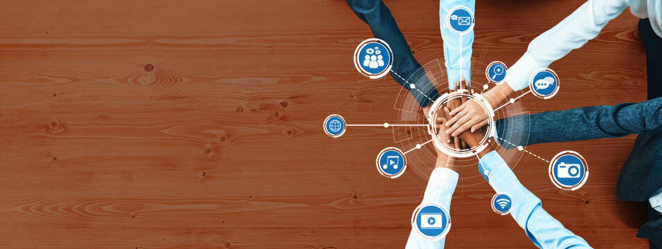 Aerial view of diverse hands joining together on a wooden surface, surrounded by social media icons, symbolizing teamwork and collaboration in digital age. Amity - Powered by Adobe