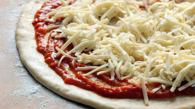 Delicious homemade pizza in preparation with vibrant red tomato sauce and fresh mozzarella cheese on dough - Powered by Adobe