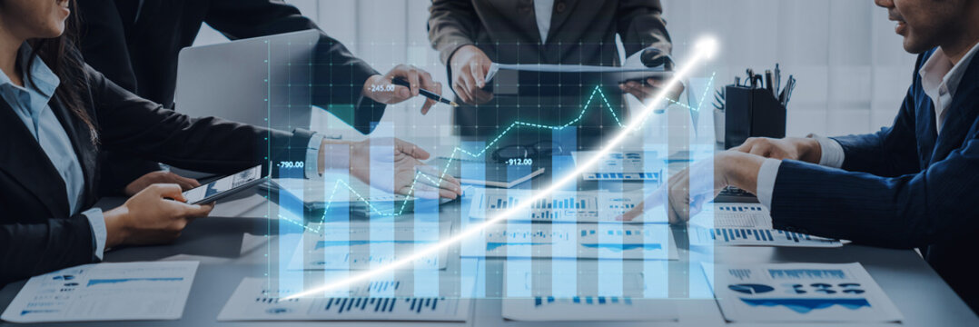 A dynamic business team collaborates in a modern office, analyzing financial data with digital tools. They engage in discussion over charts and reports. Axiom