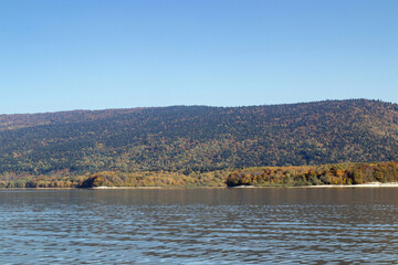 Mountain lake with gentle ripples, autumn forested hills and distant ridges under clear blue sky