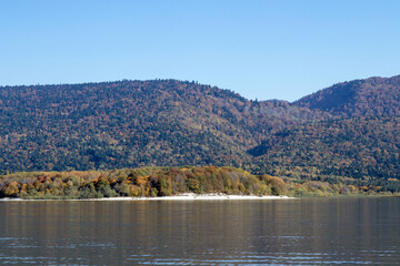 Mountain lake with gentle ripples, autumn forested hills and distant ridges under clear blue sky