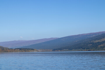 Mountain lake with gentle ripples, autumn forested hills and distant ridges under clear blue sky