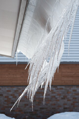 Row of dangerous icicles sliding from house roof eaves in springtime