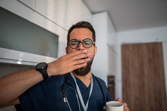 Tired male doctor yawning and drinking coffee - Powered by Adobe