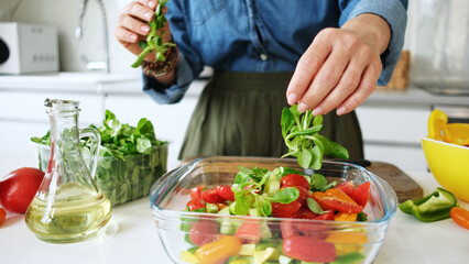 Woman Adding Greens To Salad Bowl